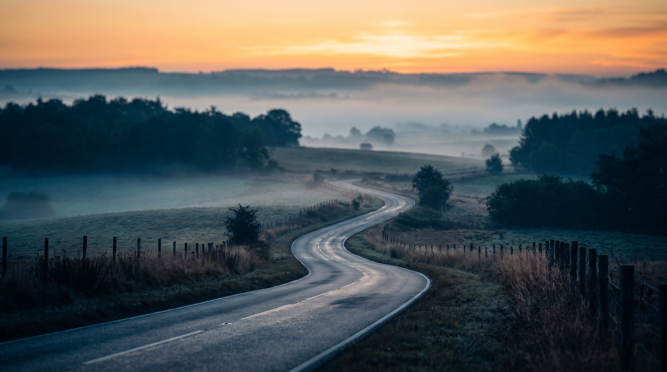 An empty road curving through open country at sunrise